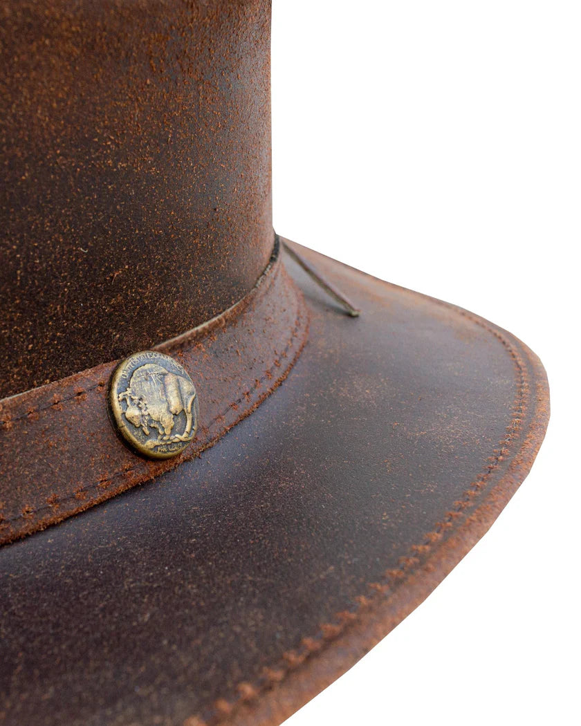 Close-up macro view of a brown distressed leather cowboy hat detailing the textured grain, stitched brim edge, and an antique buffalo nickel concho.