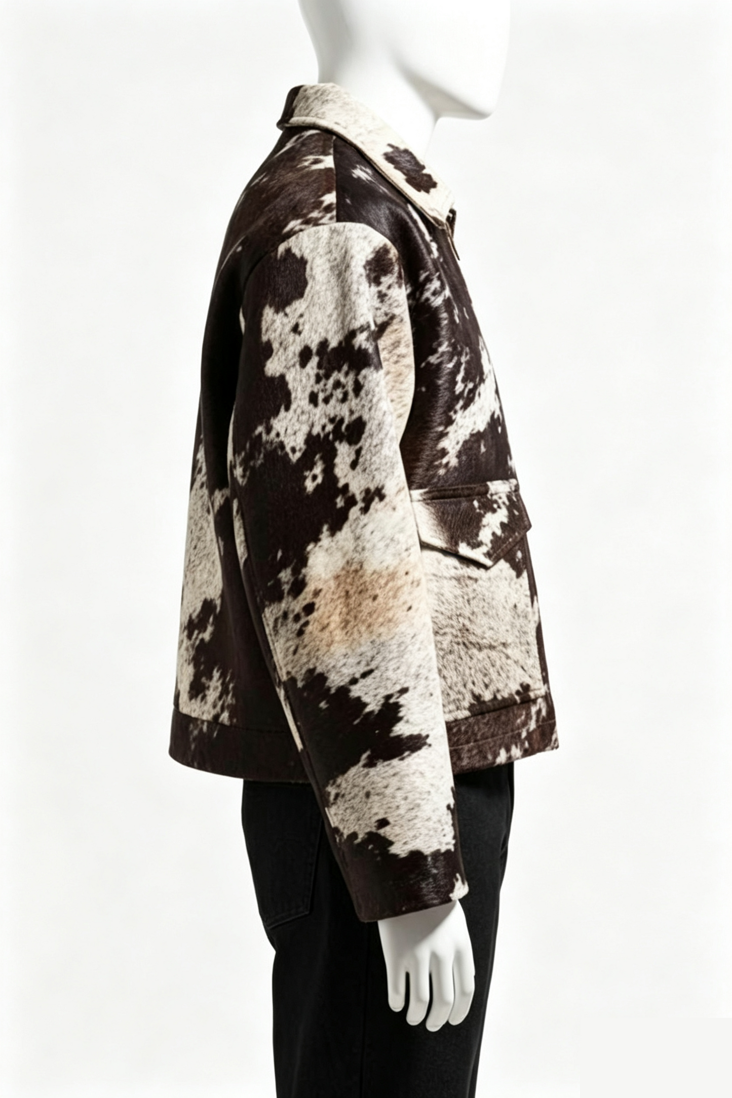 A side-profile view of a cropped jacket with a brown and cream cowhide pattern, displayed on a white mannequin against a white background.