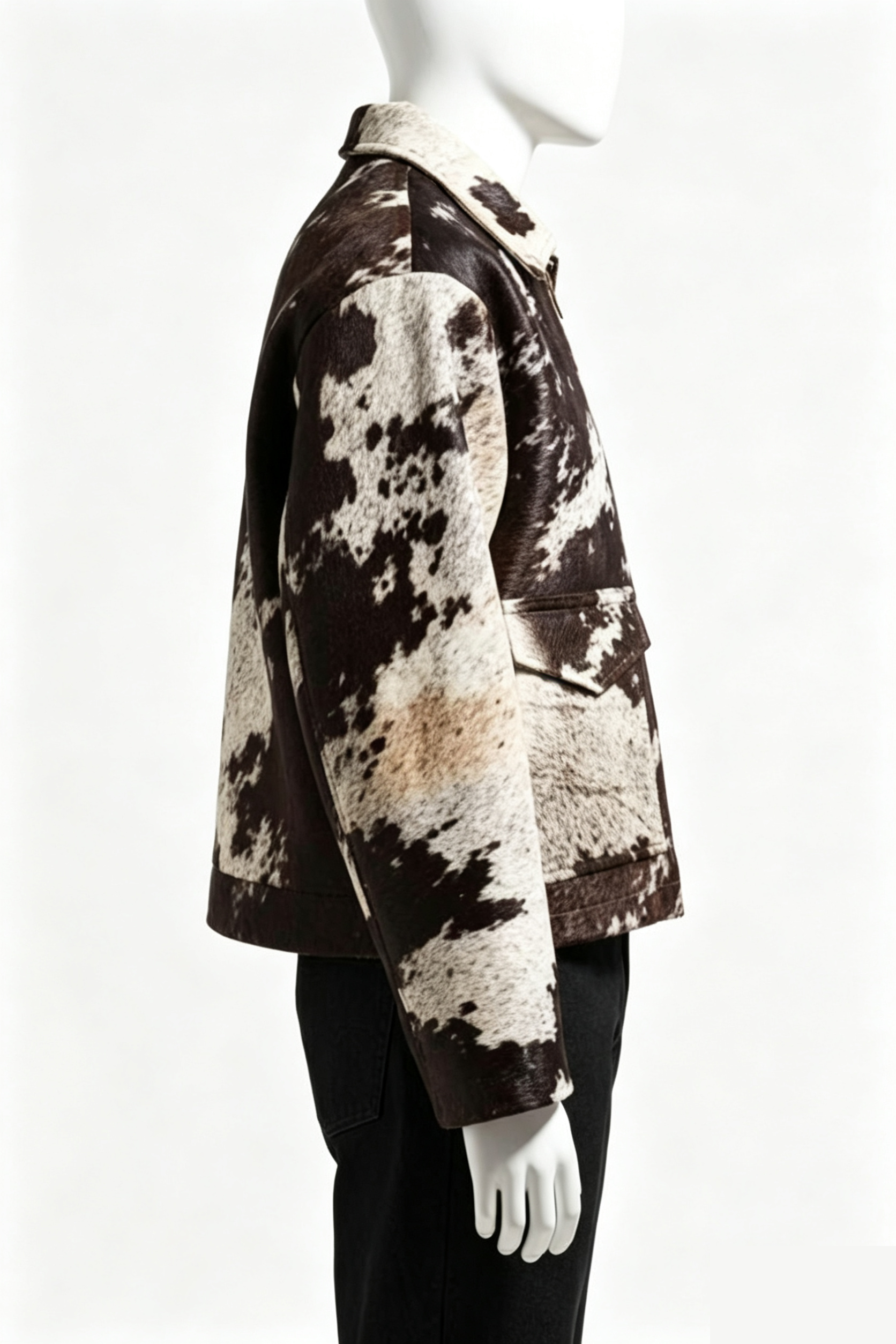 A side-profile view of a cropped jacket with a brown and cream cowhide pattern, displayed on a white mannequin against a white background.