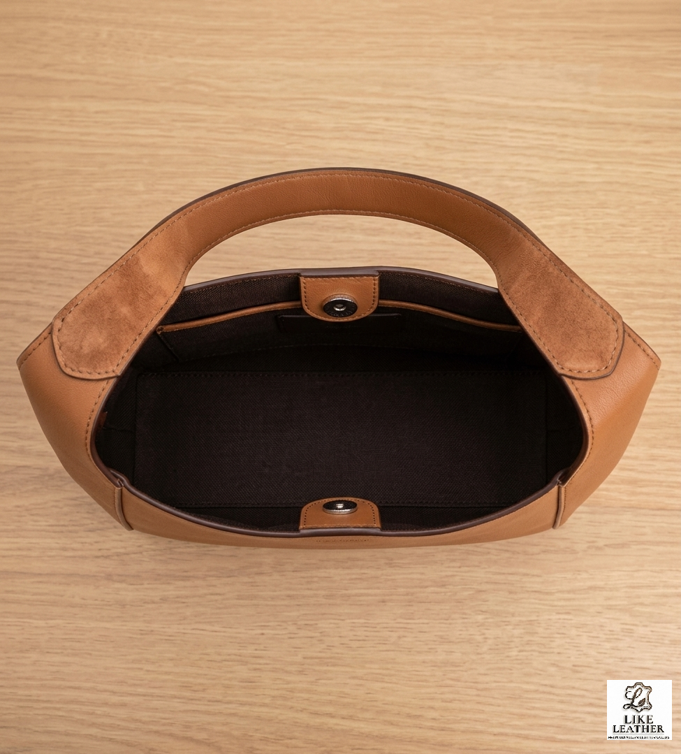 Top-down view of tan leather shoulder bag interior showing dark brown lining and magnetic snap button.