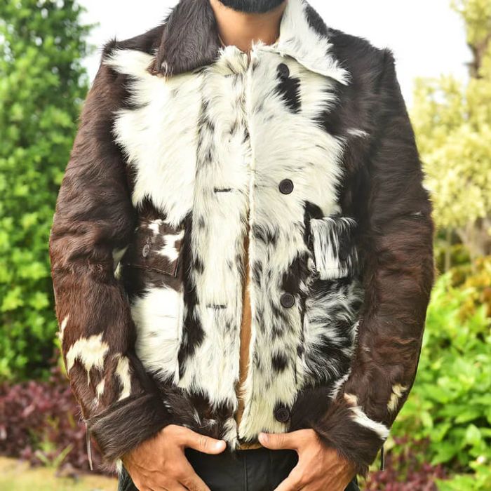 A person wearing a cowhide-style jacket with a brown and white mottled pattern, photographed outdoors with blurred greenery in the background.