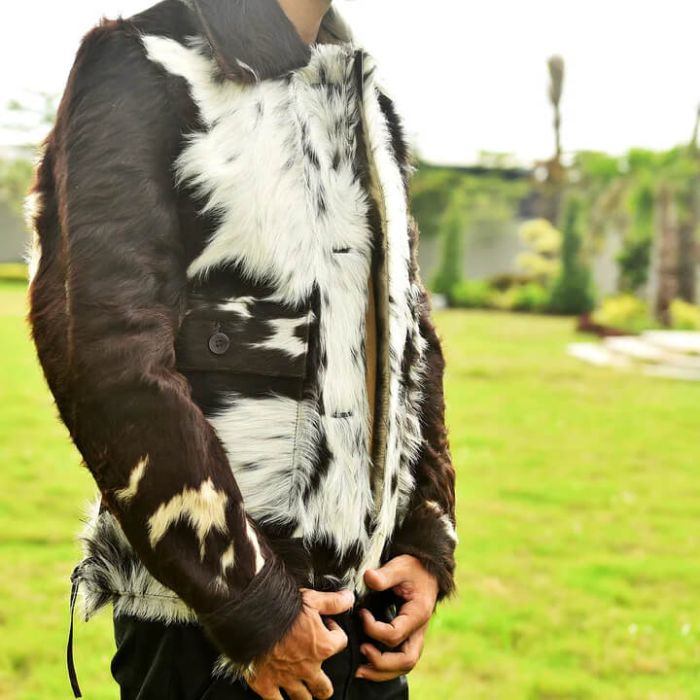 A person outdoors wearing a black and white cowhide faux fur vest with dark brown faux fur sleeves and a black collar, standing on a green lawn.