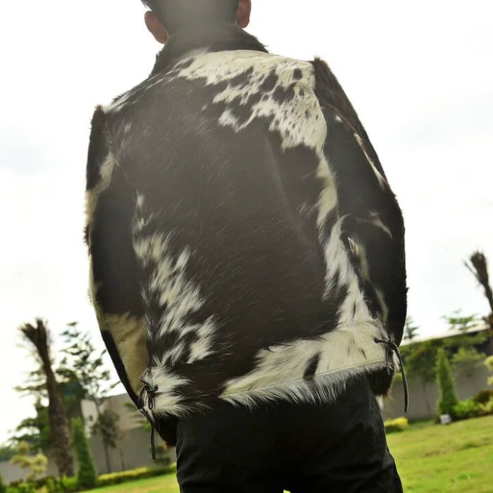 A person viewed from behind wearing a black and white cowhide jacket outdoors on a grassy lawn.